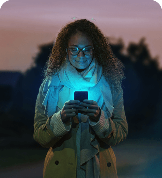 A woman gazing down at her smartphone screen, which emits a soft glow